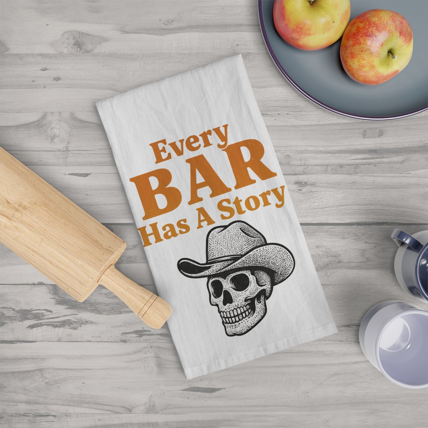 Tea towel with cowboy skull design and text 'Every Bar Has A Story' on a wooden surface.