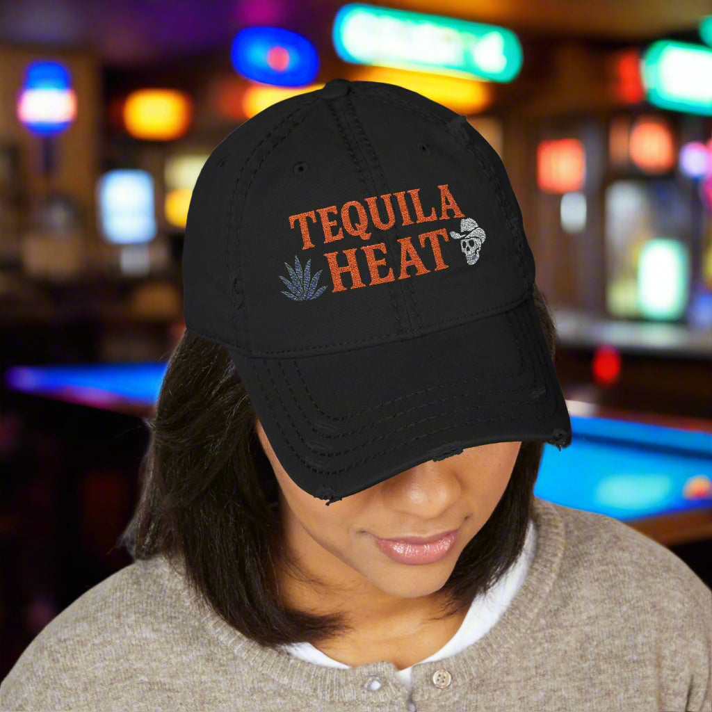 Black cap with 'Tequila Heat' text worn by a person in bar