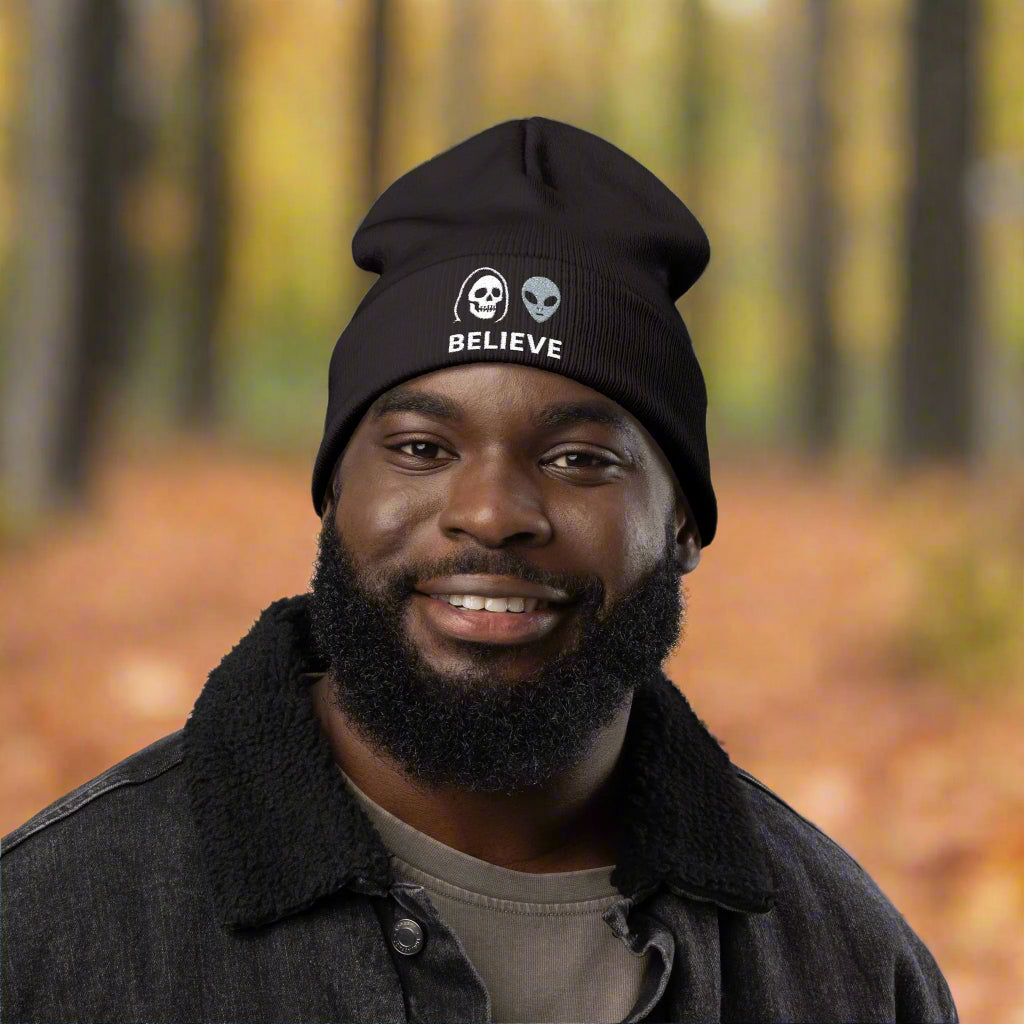 Man wearing a black beanie with a skull and alien design, and the word 'BELIEVE'.