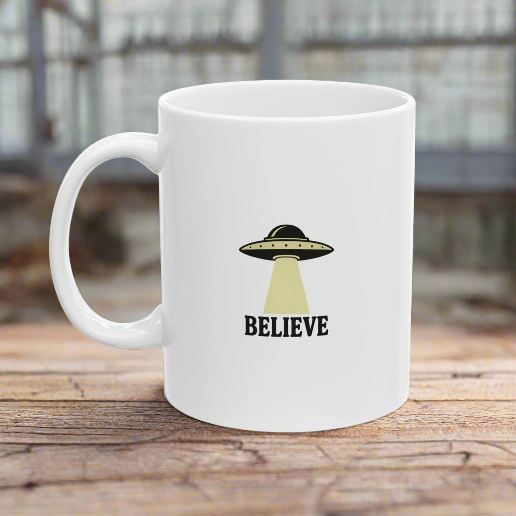 White mug with UFO design and 'BELIEVE' text on a wooden surface