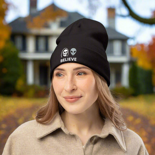 Person wearing a black beanie with alien and skull design, text 'BELIEVE' on a white background
